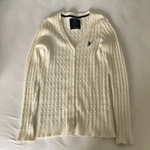 Us Polo kofta - Vit kofta från US. Polo. Köpt second hand, jag har endast använt ett par gången. Fint skick förutom en liten fläck som knabbg syns på vänter arm. Bild på fläcken på bild 2. Kan frakta om köparen betalar för frakten, pris kan diskuteras. 
