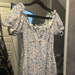 Blommig sommarklänning  - Super fin sommarklänning med blå blommor på! Köpt på Nelly i storleken M! Sitter jätte fint på kroppen, den format verkligen! 