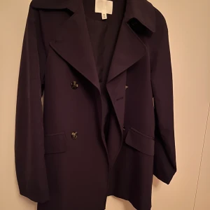 Trenchcoat kort HM xs - Kort trenchcoat från HM. Stl xs. Använd 2ggr, så absolut nyskick! Djur o rökfri. Inköpt våren 2023 för 699kr. Kraftigt matt/borstat tyg.