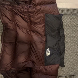 The North Face- 1996 Retro Nuptse Jacket, Brown/Black - Säljer denna jacka då jag har köpt en ny och har inget behov för denna längre. Jackan köptes hösten 2023 och är i relativt bra skick. 
