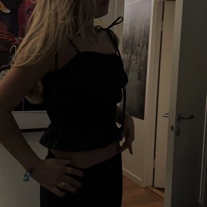 Svart topp - Svart festtopp. Smala axelband med knyte. I satin liknande material