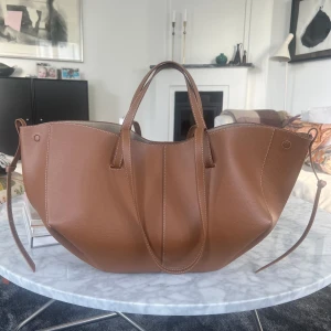 Polène väska - Polene väska i modellen Cyme. Färg: textured camel. Det är originalstorleken i nyskick, ca 1 månad gammal. Inköpt på polenes hemsida och dustbag medföljer. Kvitto finns digitalt.