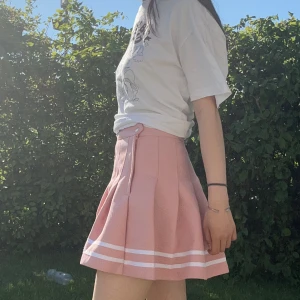 Rosa tenniskjol  - Ljusrosa tenniskjol med vita ränder längst ned. Passar perfekt till sommaren. Plagget är i använt skick, lösa trådar, se bild 4. Kjolen är från HM i Stl S men fungerar även om man har XS. 