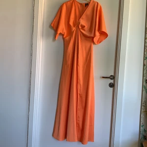 Orange maxiklänning  - Fantastisk maxiklänning med slits i en solig orange, perfekt till balen eller bröllopet. Slitsen sitter på vänster ben och ger klänningen det lilla extra.  Endast använd en gång. Superfint skick, men finns en liten fläck (bild).  Orginalpris: 599kr
