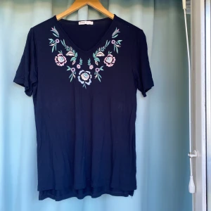 T-Shirt - Mörkblå kortärmad tröja med blommig rundad hals. Använd några gånger  67%viskos 63% elastisk 