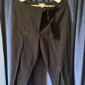 Kostymbyxor  - Svarta kostymbyxor med silverspänne de man knyter fast midjebandet, ankellånga