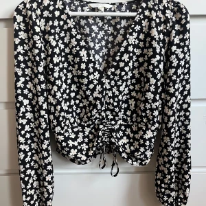 Svart blommig blus - Svart blus med vita blommor från HM. Aldrig använd men har tagit bort lappen. Har aldrig använt den då jag inte tycker att den sitter bra på mig då den är lite stor vid bysten för mig. Storlek S.  Nypris 399 säljer för 199. Kan dock diskutera pris. 