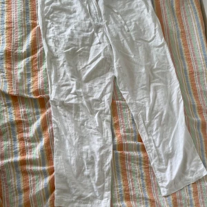 Vita linnebyxor - Ett par vita linnebyxor i storlek XL. Byxorna har en knapp och dragsko i midjan för justerbar passform. De är tillverkade av ett lätt och luftigt material, vilket gör dem perfekta för varmare väder.