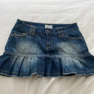 Jeanskjol från Moto - En kort jeanskjol från Moto med volangdetaljer. Kjolen har en klassisk femficksdesign och en knapp- och dragkedjestängning framtill. Den är i en blå tvättad denimfärg med slitna detaljer.