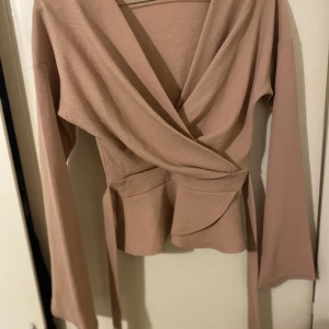 Omlottop med bälte i midjan  - Rosa omlottblus med bälte i midjan slits vid ärmarna. Går att bära off shoulder. Perfekt att bära till finare tillställning. Liten i storlek dvs passar en 36:a eller liten 38:a  