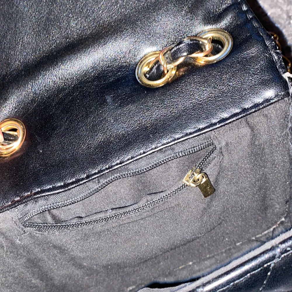Liten axelremsväska i svart med guldfärgade detaljer. Dragkedjan inuti väskan är trasig, i övrigt är väskan i gott skick.. Väskor.