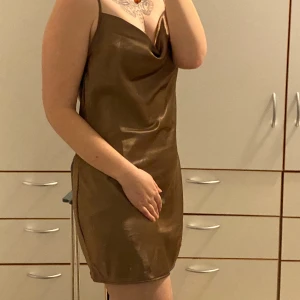 Söt brun klänning  - Skön brun klänning med något satin liknande tyg. Endast använd en gång så är i nyskick. Går enkelt att ha på sommaren då ryggen är låg med korsade straps.