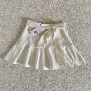 ZARA vit volangkjol med knytband - Superfin kjol med inbyggda shorts och knytband i midjan från ZARA. Ny med tags kvar, utan anmärkningar. Spana gärna in mina andra annonser. Följare får upp till 40% rabatt på allt 🌷