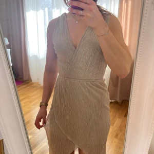 💛Plisserad guldskimrande klänning från TFNC💛 - Storlek L (Rymlig) . Se bild för materialinformation . Utan anmärkning med reservation för att jag missat någon ev tråddragning .