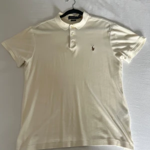 Polo Ralph lauren Piké M - Detta är min Polo piké i medium som köptes på NK någon gång under våren 2023. Färgen kan endast beskrivas som en fin nyans av vanilj vit samt att loggan på bröstet är brunt (verklighetsfärgad). Finns tyvär en mindre skada på högra axeln.