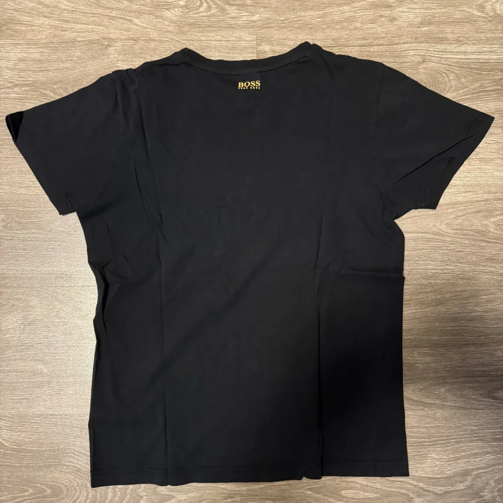 Säljer en svart Hugo Boss t-shirt i storlek M med guldfärgad logo på bröstet. T-shirten är i mycket bra skick och tillverkad av mjukt och bekvämt material. . T-shirts.
