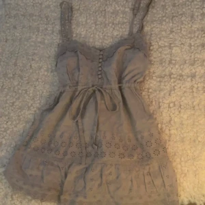 Grått linne med knappar - Linne från Vila. Använd några gånger, men har inga skador/ fläckar, förutom att snöret på linnet är synligt använd, men syns inte eftersom man knyter den!  Midjan är justerbar pågrund av snöret, och baksidan är elastisk!