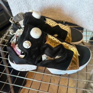 Reebok instapump Fury OG sandaler  - Riktigt snygga och sköna skor från Reebok, med instapump. Svart, vit och guld.  Cutouts och öppen tå.  Tyvärr en halv storlek för små för mig.  Storlek 37,5   350kr  