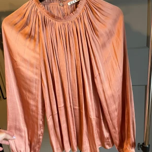 Blus från Wera  - Korallfärgad blus från Wera. Stor i modellen. Glansigt tyg likt siden.