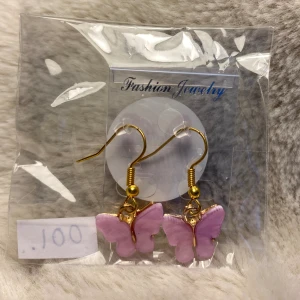 001. Nya guldfärgade örhänge med lila fjärilar, nickelfria  - Till örhängena ingår små gummipluppar att sätta på baksidan så att örhängena sitter lite bättre på plats.  Örhängena är fint inpackade i en liten cellofanpåse med ett litet klistermärke på baksidan. Perfekt att ge bort som present.