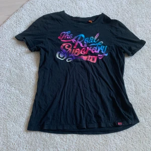 superdry t-shirt - Svart superdry t-shirt med färgglatt tryck i strl 38. Inte så använd, tvättas och stryks innan den skickas! Ca 51 cm lång💞