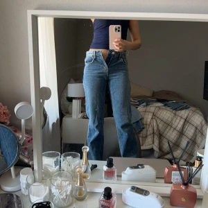 Blå jeansbyxor - Ett par blå jeansbyxor med hög midja och rak passform. Byxorna har en klassisk design med fem fickor och knappgylf.