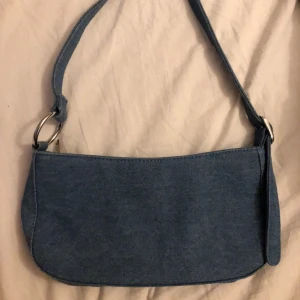 Handväska - En så söt handväska i denim material. Har två fack på insidan, ett stort och ett litet, syns på bild två. Aldrig använd så i nyskick. 