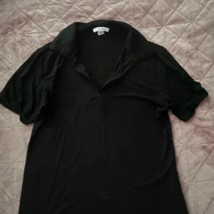 Svart blus från H&M - En svart blus från Newyorker med korta ärmar och en klassisk krage. Blusen har en enkel och elegant design, perfekt för både vardag och fest.