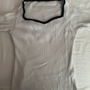 Vit ribbad tröja med svart kant - En vit ribbad tröja med en svart kant runt halsen. Tröjan har långa ärmar och en unik halsringning.