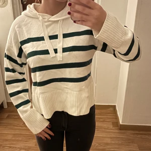Kroppad vit stickad tröja med gröna streckmönster och luva, storlek XS 🤍💚 - Säljer en kroppad vit stickad tröja i storlek XS med gröna streckmönster och luva på baksidan. Den är både trendig och bekväm, perfekt för en stilren och avslappnad look. Tröjan är i bra skick och klar för en ny ägare.