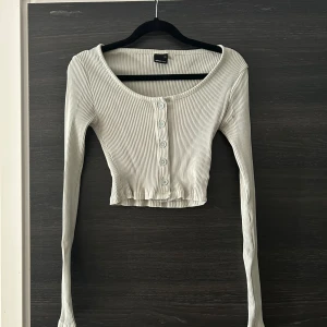 Grön tröja  - En grön, ribbstickad tröja med långa ärmar och knappar framtill. Tröjan är cropped och har en rund halsringning.