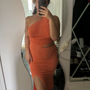 Orange klänning - En orange klänning med en axelbandslös design och en slits. Klänningen har en tight passform och är tillverkad i ett material som ser ut som sammet, men är polyester💕 använd 1 gång