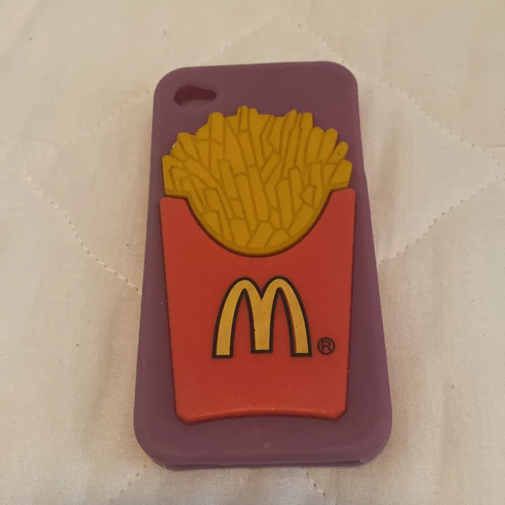 Ett lila mobilskal med en design av en röd pommes frites-förpackning med gula pommes frites. Förpackningen har en gul logotyp på framsidan.. Väskor.