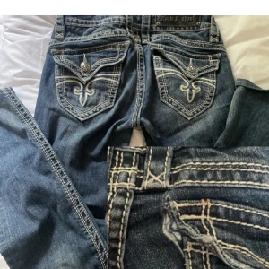 Rock revival jeans lowwaist bootcut - Rare rock revival jeans🖤 finns inte längre att köpa, nypris runt 2000! Midjamått: 35cm + lite stretch. Ytterben: 97cm. Innerben: 77cm. gylf/rise: 19cm. Strl w26/ eu34-36 finns små slitningar men bra skick! Använd köp nu eller kontakta för mer info💞 