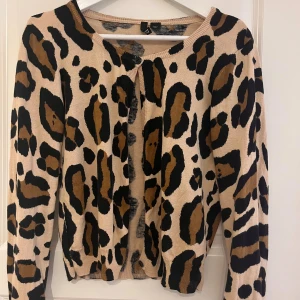 Beige leopardmönstrad kofta - En beige kofta med leopardmönster i svart och brunt. Koftan har långa ärmar och ribbstickade muddar vid ärmslut och nederkant.