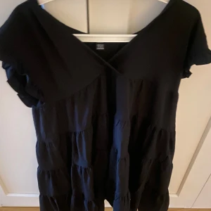 Svart klänning - En svart klänning med korta ärmar och volangdetaljer. Klänningen har en lös passform och något kortare än knälång på mig (164cm)