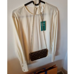 NY NWT Blus - Lyxig blus som ser otroligt exklusiv ut, en dröm att bära.  Dekorativ keyhole i nacken som knäpps med likadana guldknappar som vid ärmsluten.  Size 34/36