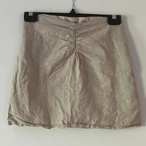 Beige linnekjol med lite skrunch på framsidan  - Fin linnekjol från Gina Tricot som endast är använd 2 gånger. Den har en dragkedja på sidan så att man kan få av och på sig den. Den är inte genomskinlig då den har en underkjol. (Jag kan stycka den innan den skickas)