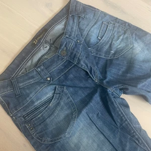 Lågmidjade bootcut jeans - SJUKT SNYGGA LÅGMIDJADE BOOTCUT JEANS!! ☀️💕🫶  Det är snygga detaljer överallt på jeansen, låren har små hål (inte helt igenom), knappen har en liten blomdetalj, fram& bakfickorna är super unika och coola. Står ingen storlek men de passar 44/46 ❤️ 