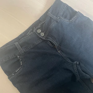 Lågmidjade jeans - Sjukt snygga jeans, med massor av snygga detaljer överallt, fram& bakfickor och runt midjan!! Lågmidjade bootcut med två knappar. Storlek 48 men de är insydda i midjan så de är storlek 42/44. Mörkblåa med lite grå nyans 💕🫶