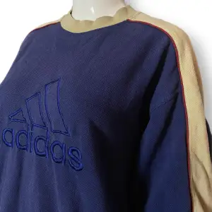 En sweatshirt i engelsk storlek 38/40 från Adidas. Skicket är 7/10 för sin ålder. Finns några slitningar på framsidan. Röda ränder längs ärmarna, syns på sista bilden. Lite mer mörkblå i verkligheten än vad det ser ut som på första bilden. 