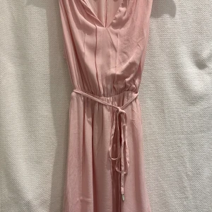 Fin rosa klänning från Mango - Ljusrosa klänning från Mango Suit.  Två lager och knytande i midjan.  Slitage enligt bild, litet märke i underkant som knappt är märkbart (se bild).   Strl. XS