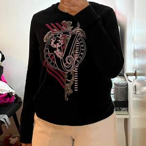 En fin Versace sweatshirt dom är svart med lite rosa detaljer. Perfekt nu till våren när man vill ha på sig något lite tjockare men ändå fräscht. 