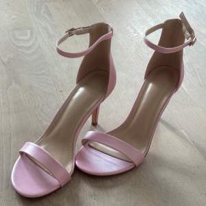 Storlek 38. Klackhöjd 7-8cm. Oanvända sandaletter i rosa nästan lite pärlskimrande färg. Ett minimalt skav i ena klacken (bild 5).