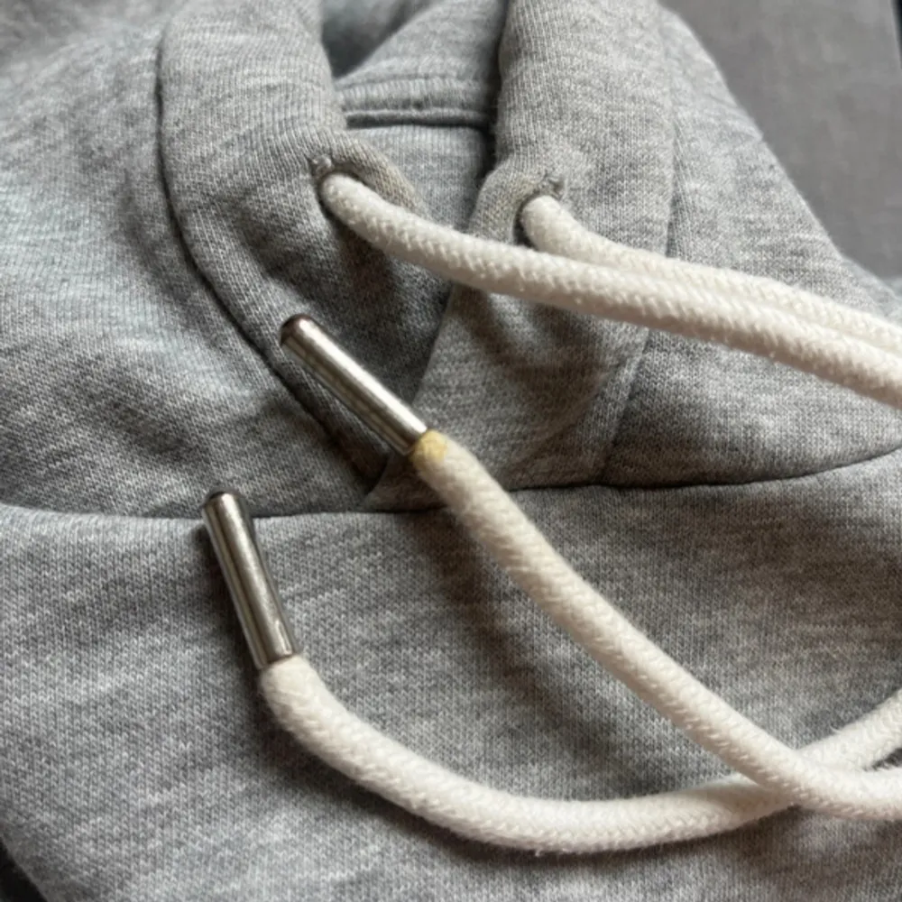 En grå hoddie från H&M i storlek M. Bra skick men lite sliten och en fläck vid snöret som man ser på andra bilden. Men annars är snörena snygga och liknar skosnören. . Hoodies.