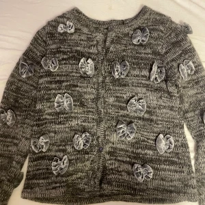 Kofta med rosetter  - Jättesöt grå kofta med rosetter, har ett litet hål på framsidan men syns knappt med rosetten framför💗