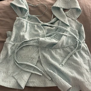 Ljusblå topp - Topp med knytning fram. Oanvänd då den aldrig Kom  till användning,