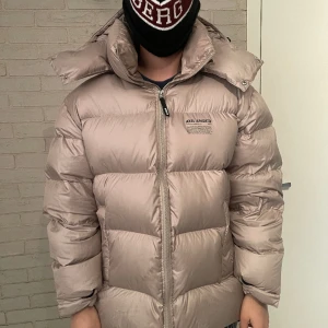 Axel Arigato Jacka - Axel Arigato dunjacka i färgen beige, håller en otroligt varm. Storlek L och toppskick, 10/10! Använd ett fåtal gånger. Luvan går att ta av och på, samt dragkedjor på sidan som gör att det kan luftas. Köpt för 5500 kr och produceras inte längre!