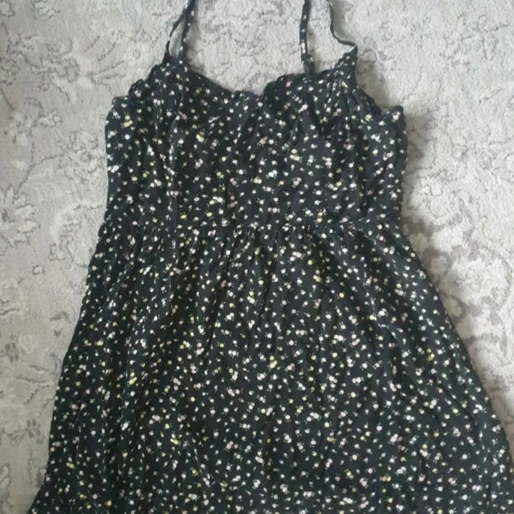 Blommig klänning med gula och rosa blommar, svart klänning. Storkel 38/M från H&M i mycket bra skick.  Har en smockad rygg och justerbara band. Klänningar.