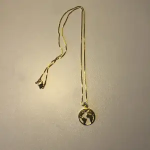 Halsband i platerat guld med ett motiv av jordklotet. Superfint och aldrig använt.
